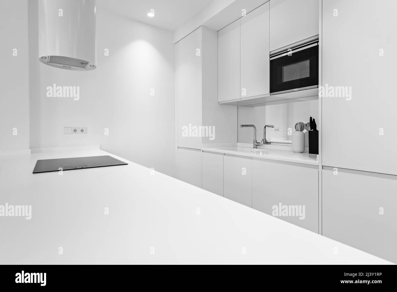 Designer-Küche mit glatten weißen Linien, integrierten Geräten und weiß lackierten Möbeln Stockfoto