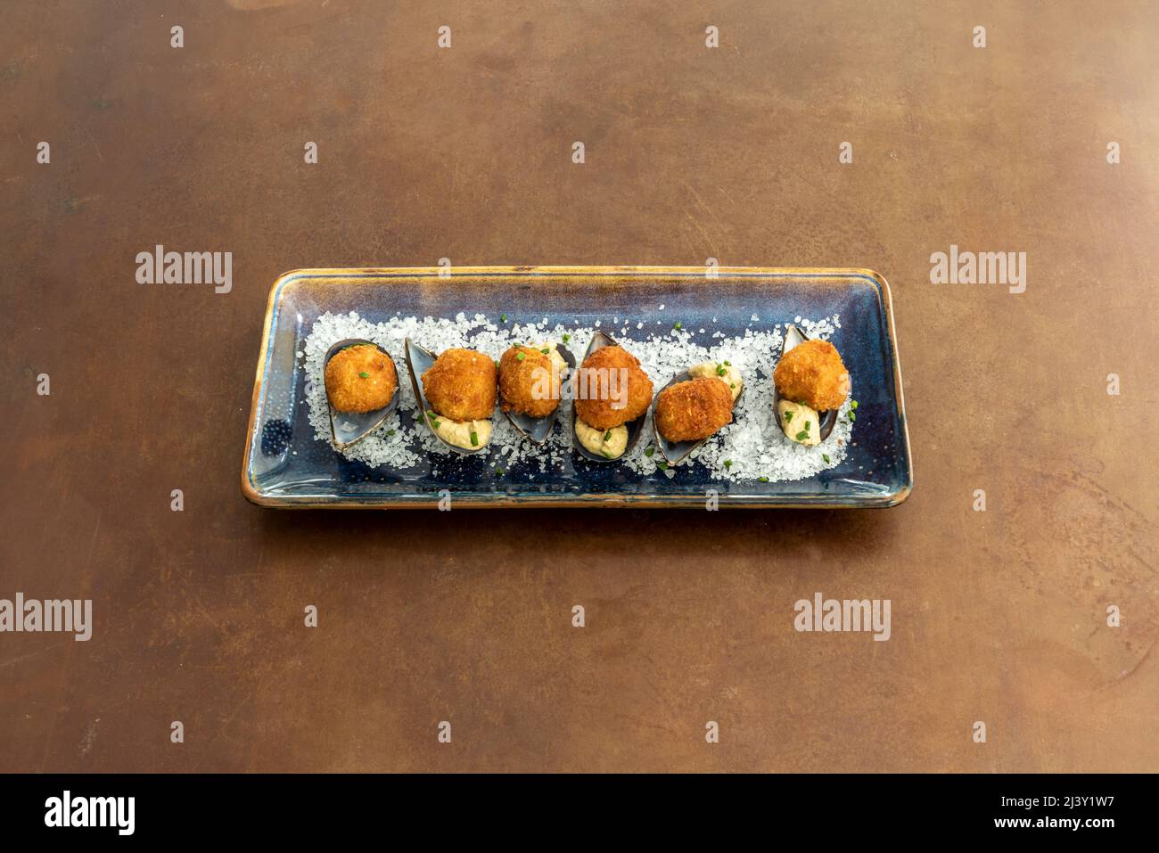 Köstliche Garnelen-Kroketten serviert marine Stil auf Muschelschalen, grobes Salz und einem blauen Teller Stockfoto