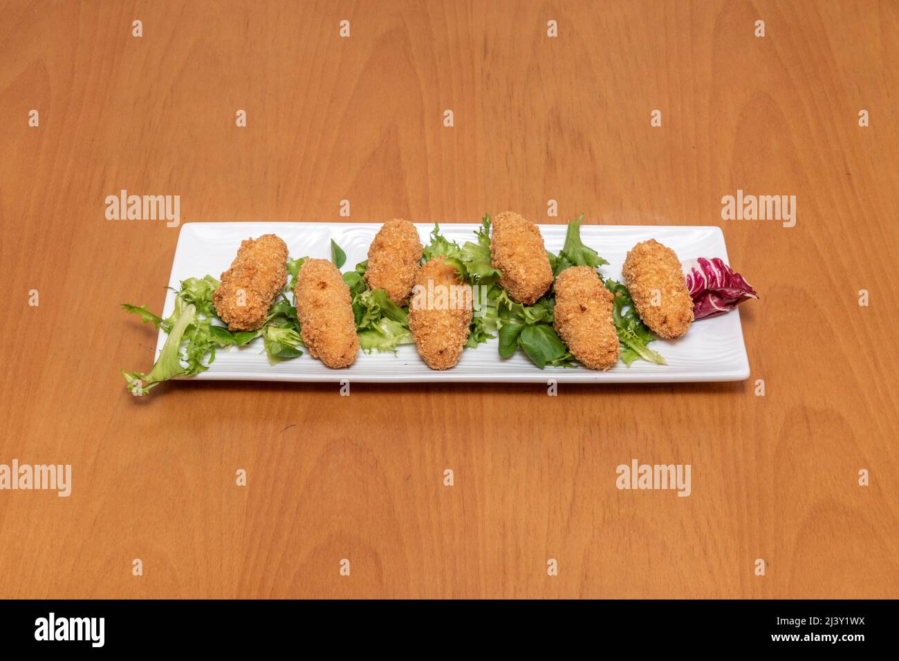 In einem spanischen Tapas-Restaurant werden köstliche und typisch spanische Kroketten mit serrano-Schinken auf einem Kopfsalat serviert Stockfoto