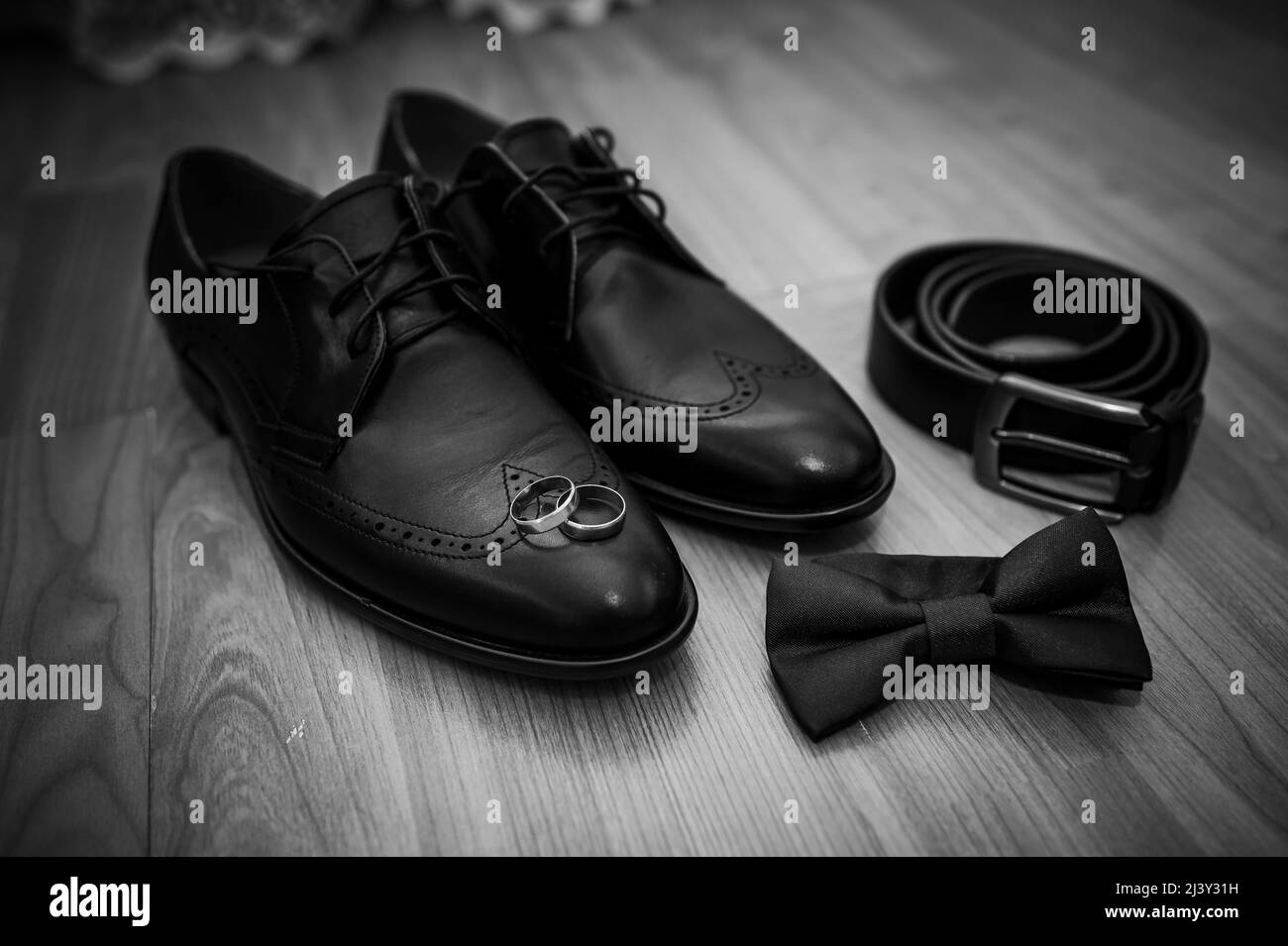 Schwarze Lederschuhe, ein Gürtel, ein Paar goldene Ringe, eine grüne Schmetterlingsband auf einem Hintergrund Stockfoto