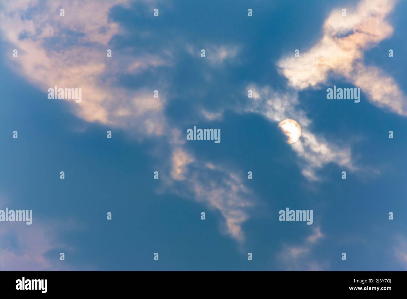 Nahaufnahme des blauen bewölkten Himmels am Mittag, mit der Sonne, die von der Wolke überstrahlt wird Stockfoto