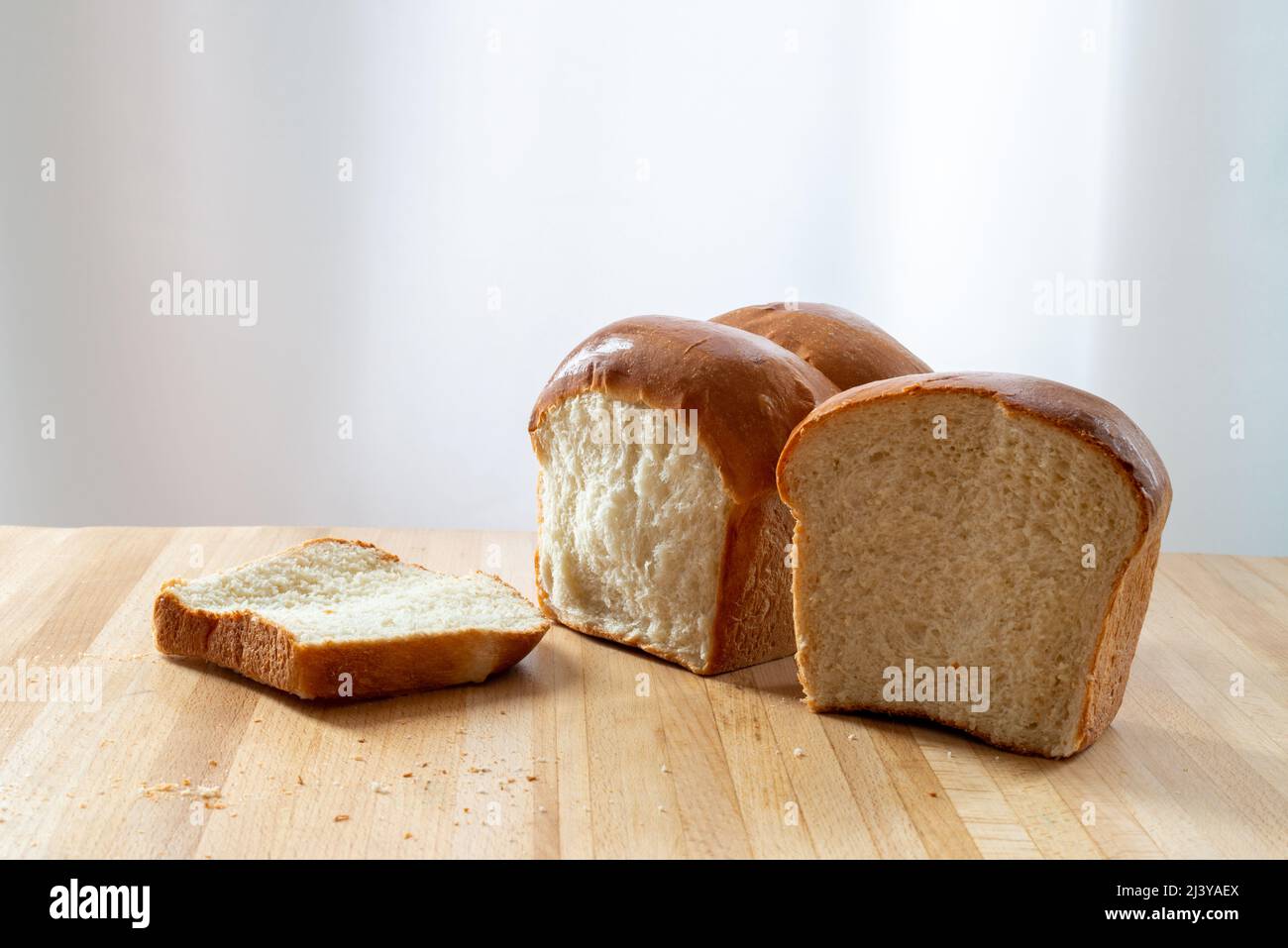 Ein einziger Laib frisches Weißbrot auf einem hölzernen Schneidebrett in einer Küche. Das warme knusprige Brötchen hat Butter über dem knusprigen Brot geschmolzen. Das Brötchen wird geschnitten Stockfoto