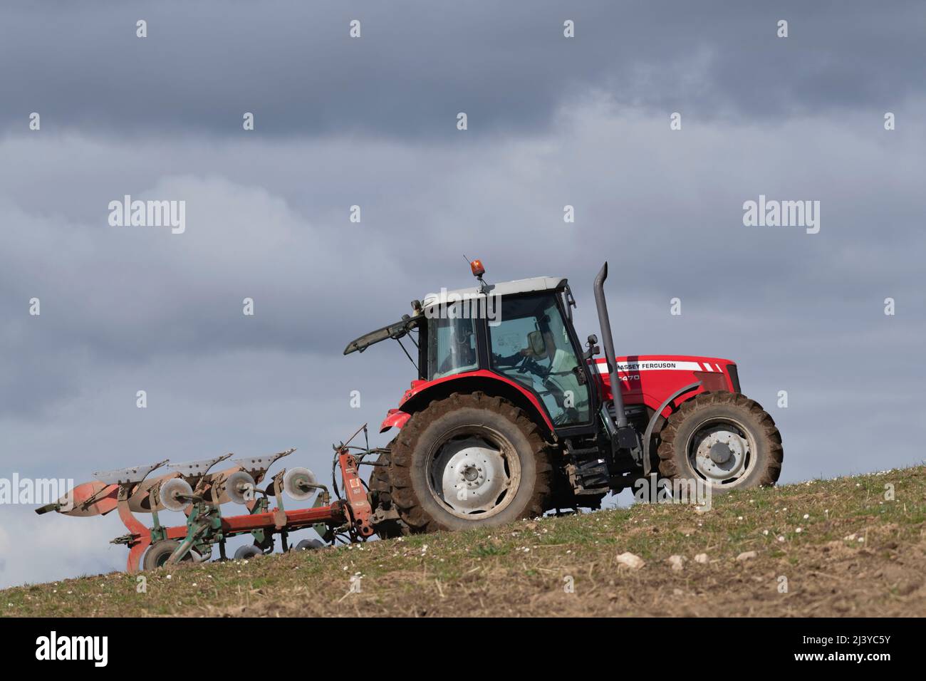 Ein Red Massey Ferguson 5470 Traktor, der an einem sonnigen Tag auf einem Rasenfeld bergauf pflügt Stockfoto