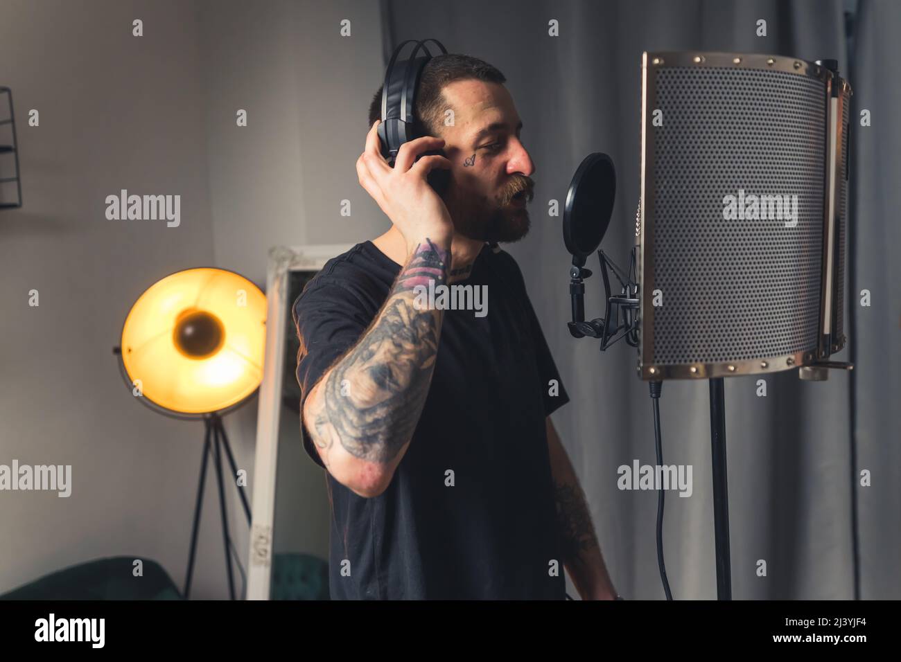 Mittlere Innenaufnahme eines europäischen tätowierten Musikers in einem Studio, das sein Rap-Album mit professioneller Ausrüstung aufnahm. . Hochwertige Fotos Stockfoto