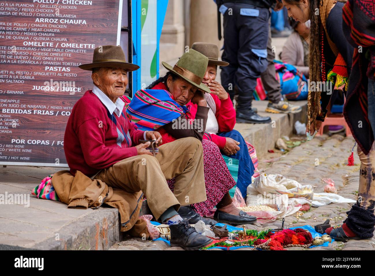 Peruanische Menschen, indigene Männer und Frauen, sitzen auf dem Bürgersteig auf dem Pisac Sunday Market im Heiligen Tal, Peru. Stockfoto