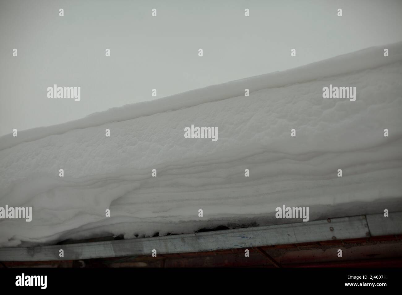 Schnee auf dem Dach. Schneebedeckter Winter. Eisschicht an der Wand angesammelt. Nach dem Schneesturm. Stockfoto