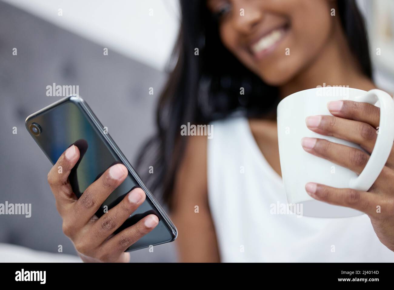 Den Tag mit Kaffee und einem Text von Babe beginnen. Aufnahme einer Frau, die ihr Mobiltelefon und eine Tasse Kaffee in der Hand hält, während sie zu Hause sitzt. Stockfoto