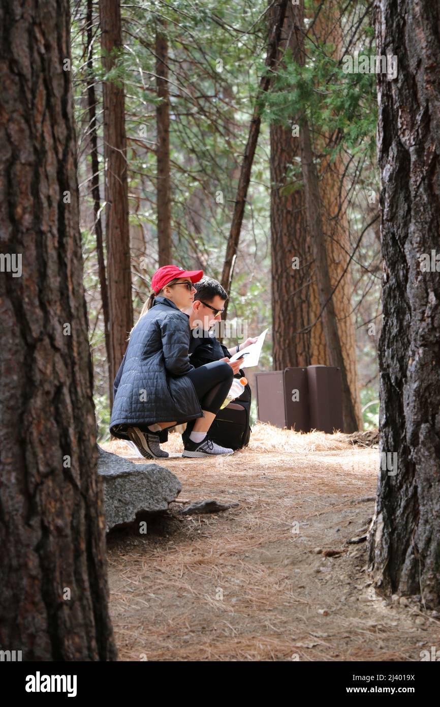 Yosemite National Park, CA - 26. März 22: Junge kaukasische Paare machen eine Pause auf einer Wanderung auf einem Pfad, um sich eine Karte anzusehen, Yosemite National Park, CA. Stockfoto