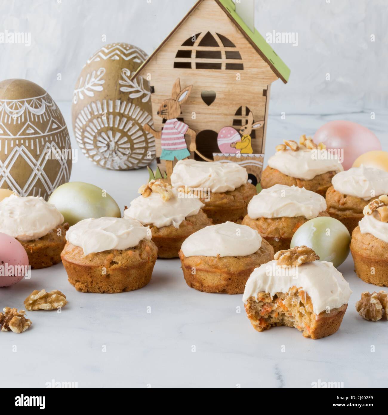 Karottenkuchenmuffins mit Frischkäse-Glasur und Osterdekorationen hinten. Stockfoto