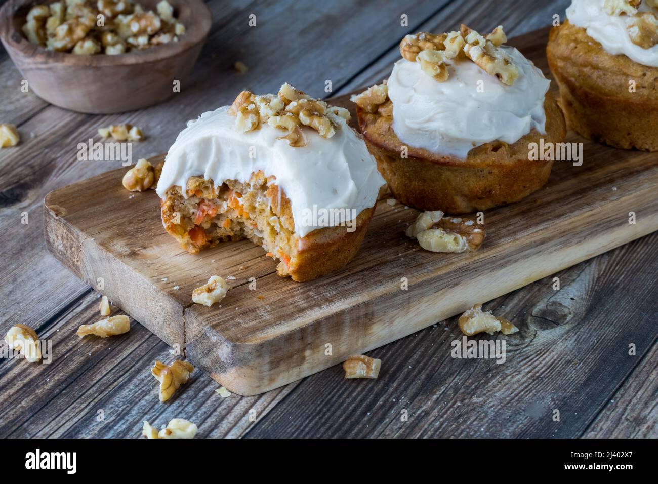 Karottenkuchenmuffins mit Frischkäse-Glasur und Walnüssen auf einem kleinen Holzbrett. Stockfoto
