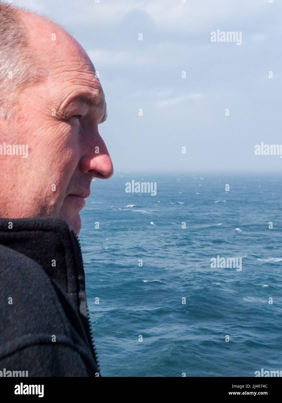 Ein Mann blickt über die Weite der Irischen See unter den Wolken eines bewölkten Tages. Stockfoto