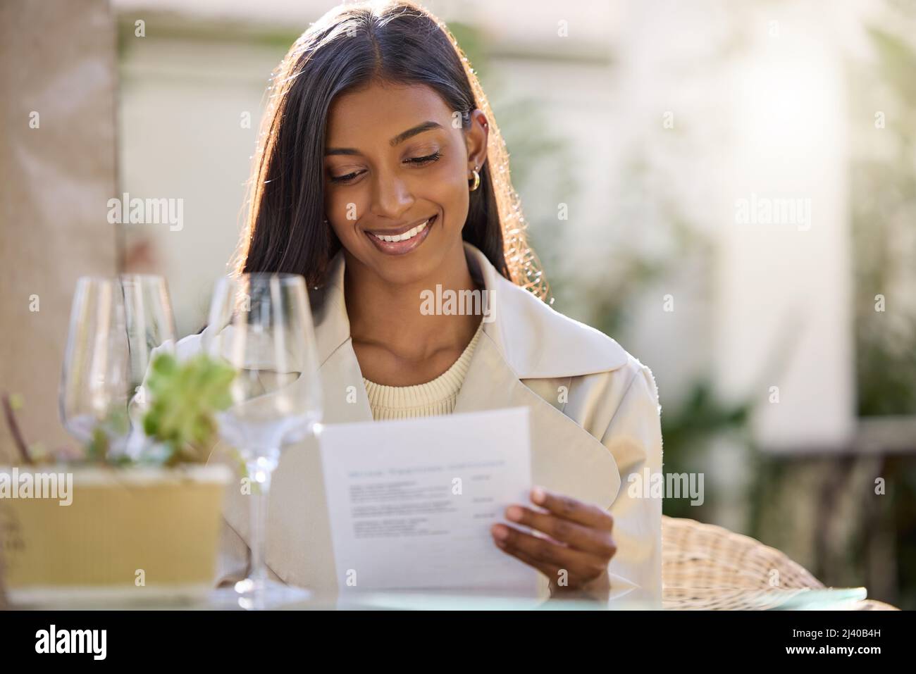 Was sollte ich haben. Aufnahme einer attraktiven jungen Frau, die alleine sitzt und während einer Weinprobe das Menü anschaut. Stockfoto