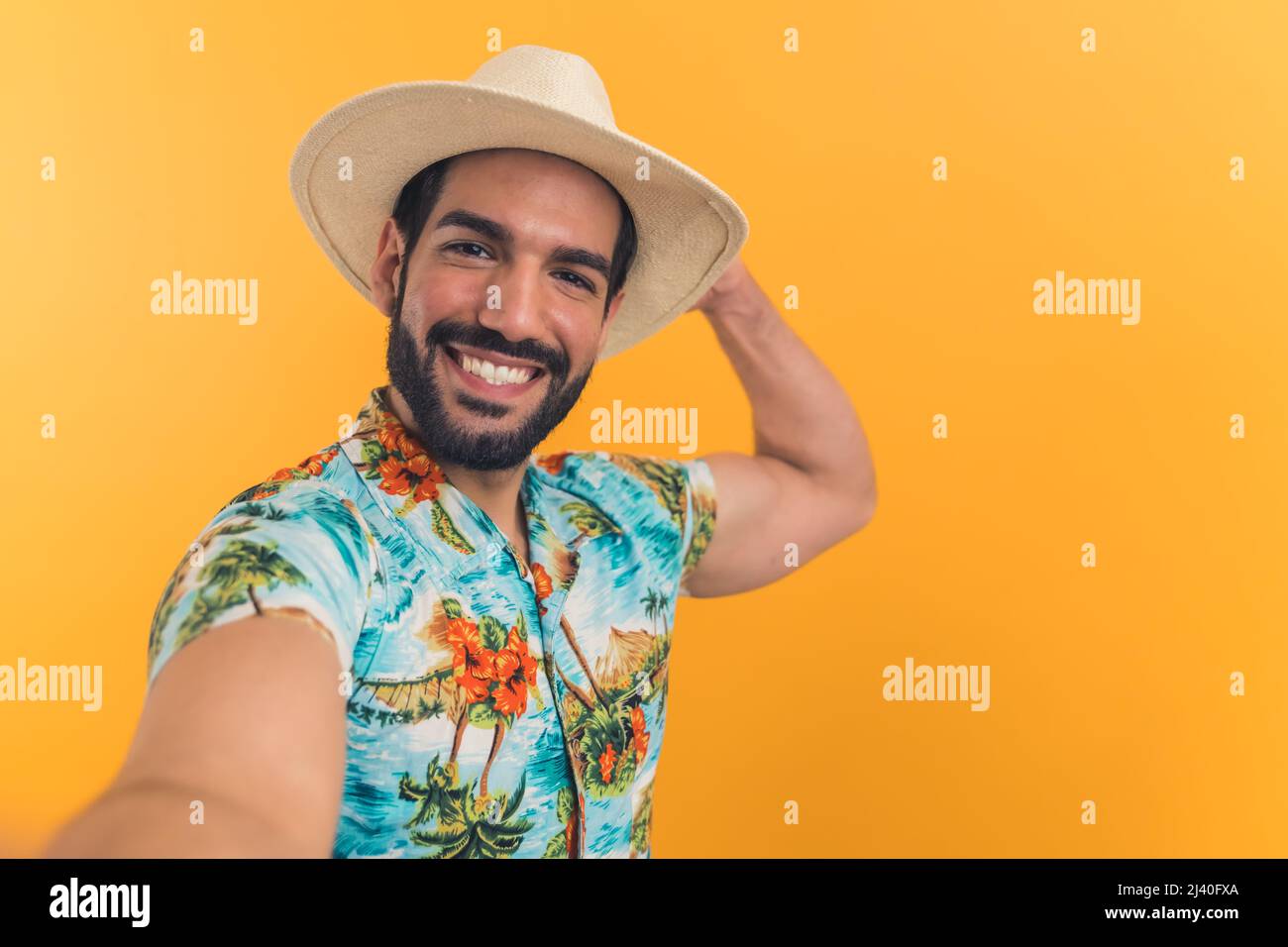 Weitwinkelansicht eines jungen lateinischen Mannes in Sommerkleidung, der seinen Arm ausstreckte und ein Selfie machte, während er seinen Hut hielt. Hochwertige Fotos Stockfoto