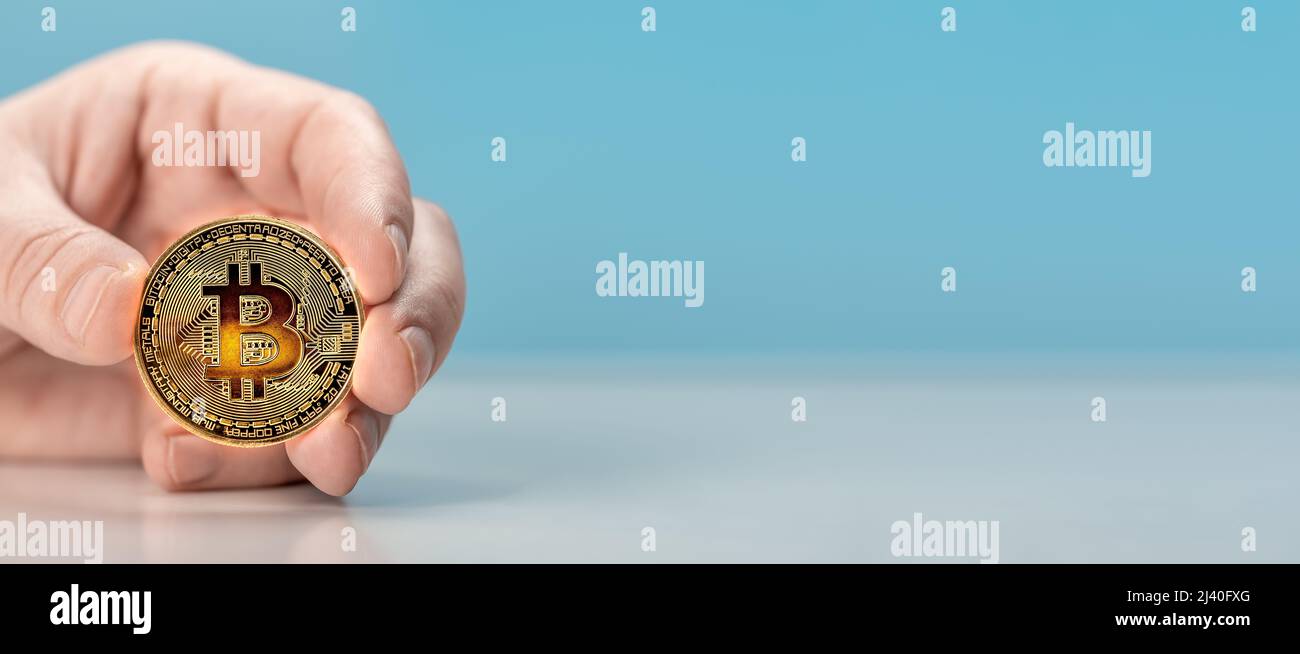 Mann Hand halten Bitcoin. Physische Bitmünze. Digitale Währung. Kryptowährung. Goldene Münze mit Bitcoin-Symbol auf hellblauem Hintergrund. Kopierraum Stockfoto