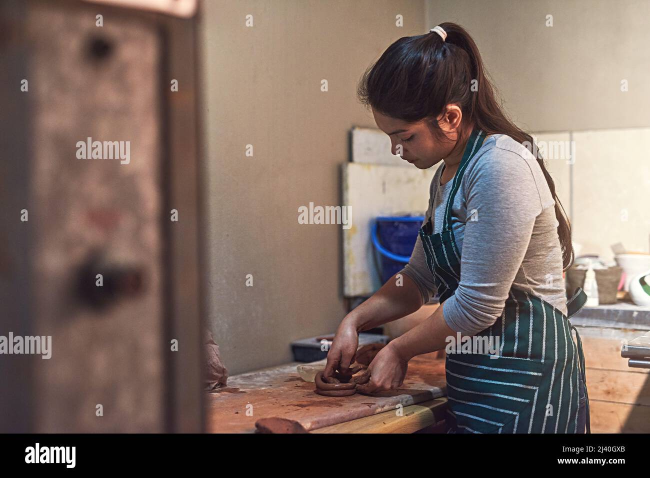 Mit Präzision und Sorgfalt basteln. Aufnahme einer Keramikkünstlerin, die in einer Werkstatt an ihrer Töpferei arbeitet. Stockfoto