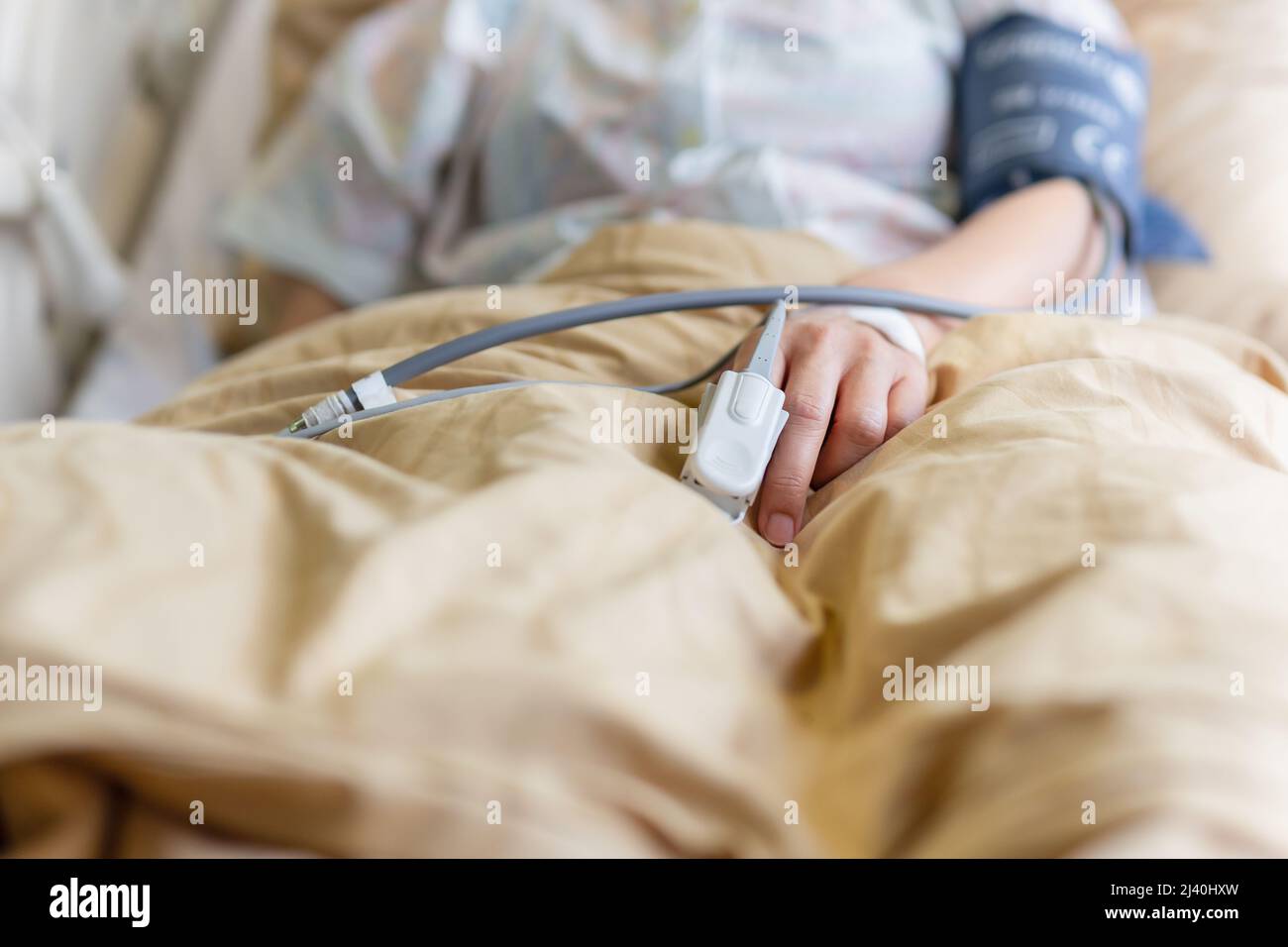 Die Hand eines asiatischen Patienten mit einem am Finger angebrachten Pulsoximeter im Krankenhauszimmer. Stockfoto