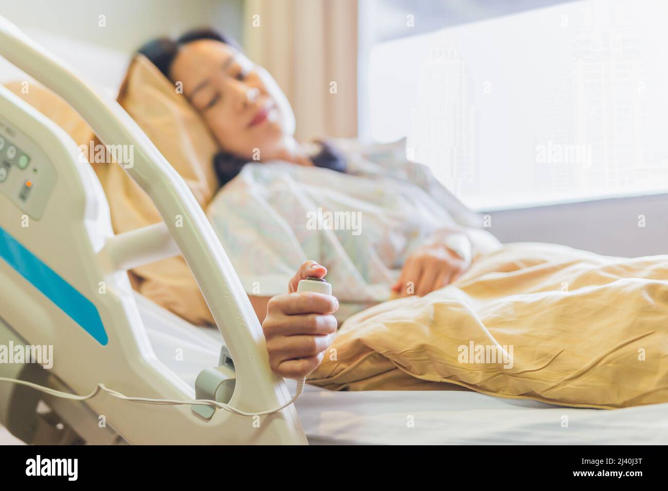 Patientin, die die Notruftaste gedrückt hat, während sie im Krankenhausbett liegt. Stockfoto