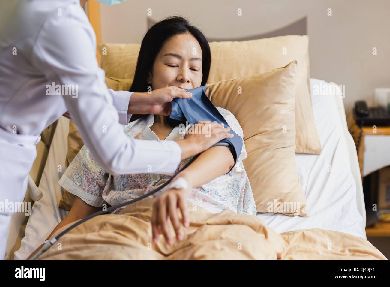 Krankenschwester, die den Blutdruck eines erwachsenen weiblichen Patienten im Krankenhausbett einnahm. Stockfoto