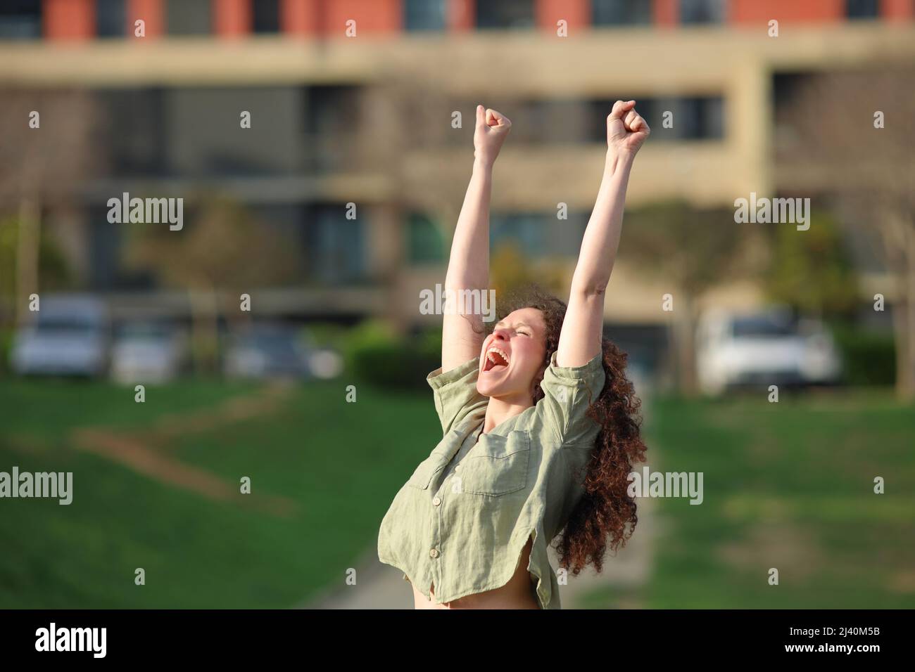 Eine aufgeregte Frau, die die Arme hebt und den Erfolg in einem Park feiert Stockfoto