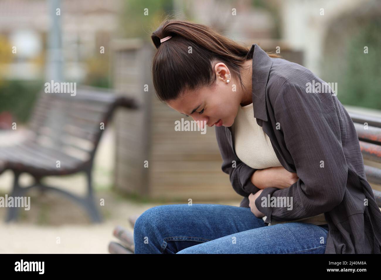 Profil einer jungen Frau mit Bauchschmerzen, die auf einer Bank in einem Park sitzt Stockfoto
