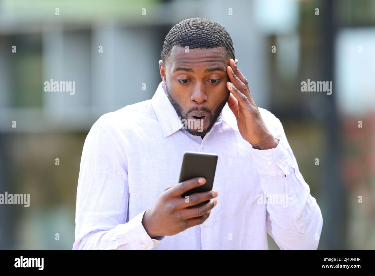 Vorderansicht Porträt eines überraschten Mannes mit schwarzer Haut, der Nachrichten auf der Straße am Telefon liest Stockfoto