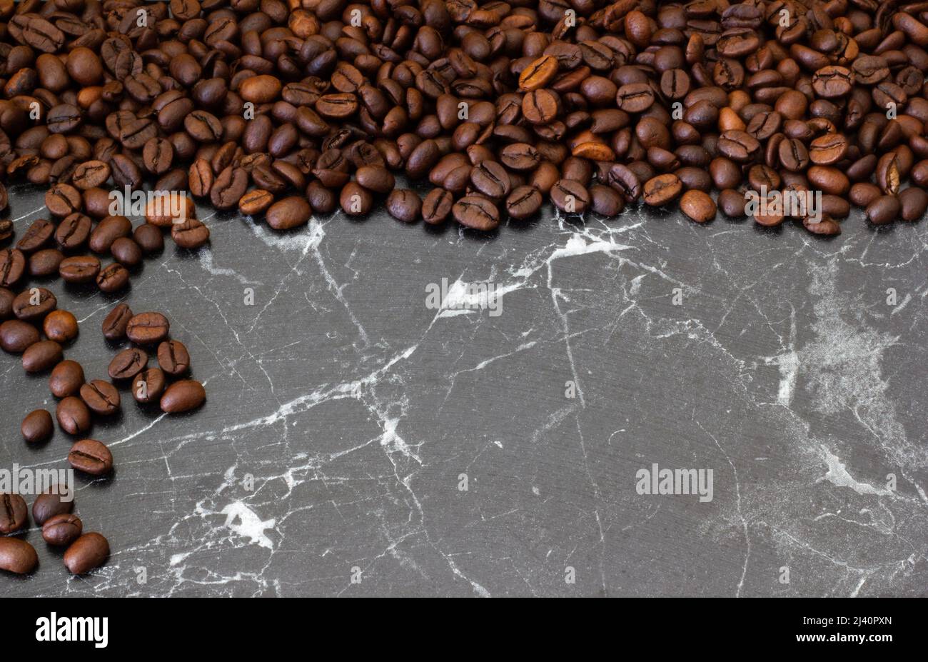 Draufsicht auf Stapel gerösteter Kaffeebohnen, die aus grauem Boden verschüttet werden. Kann als Hintergrund oder Textur verwendet werden. Stockfoto