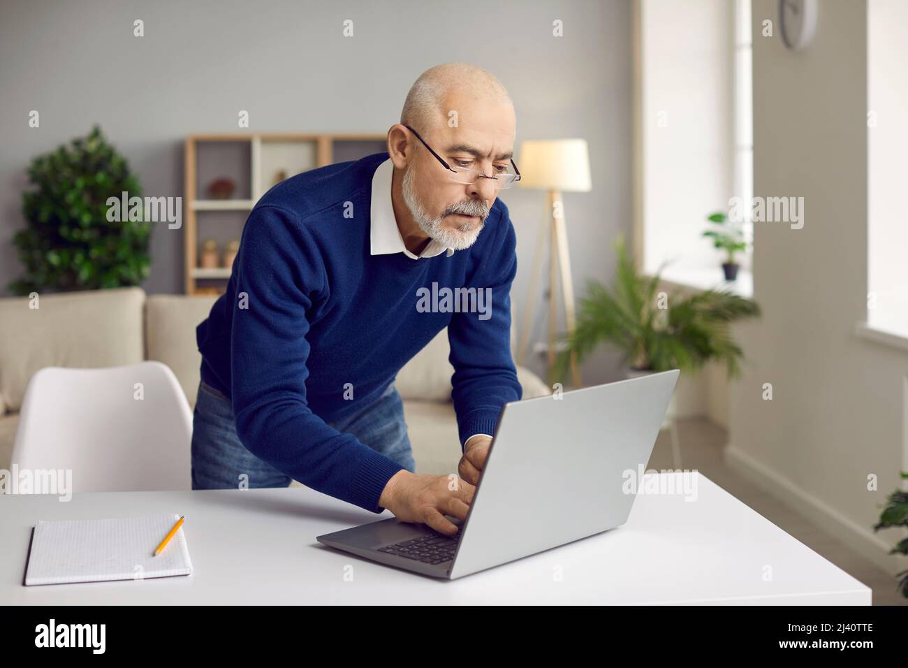 Seriös leitender Geschäftsmann in einer Brille, die an seinem Schreibtisch steht und seinen Laptop benutzt Stockfoto