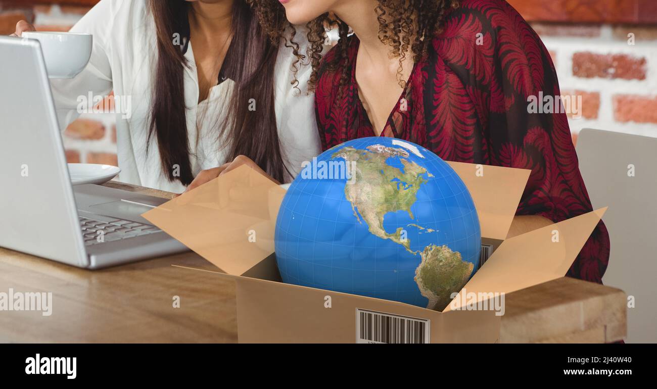 Globe im Lieferkarton gegen den mittleren Teil von zwei Frauen, die einen Laptop in einem Café benutzen Stockfoto