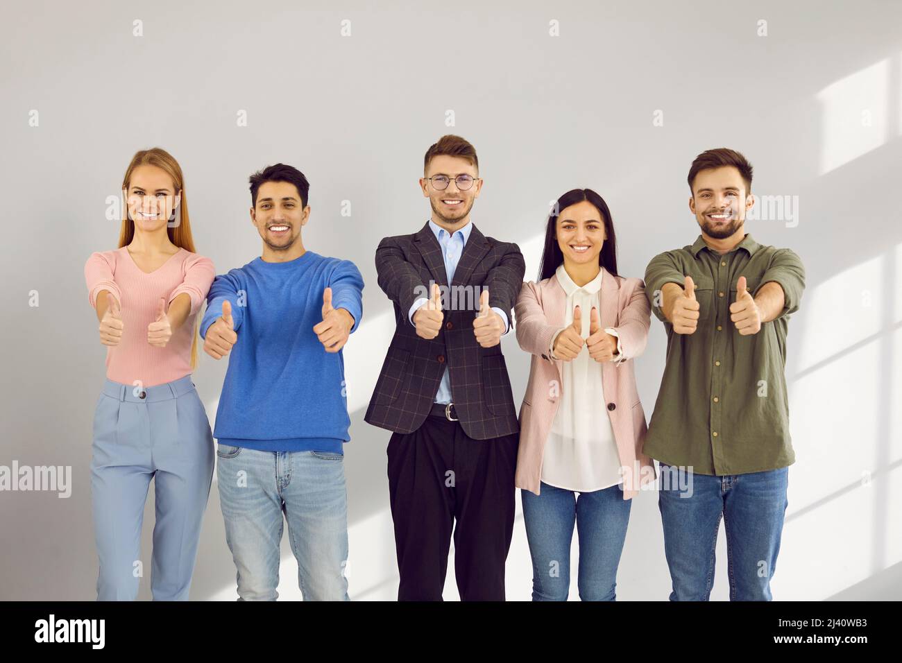 Porträt aktiver und intelligenter junger Menschen, die mit Daumen nach oben zeigen, um sie zu genehmigen oder zu empfehlen. Stockfoto