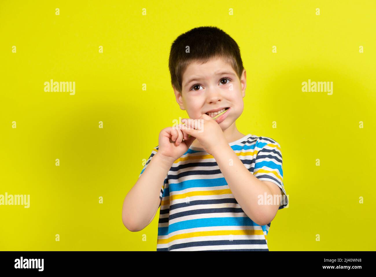 Ein kleiner Junge putzt seine Zähne mit einer Zahnbürste auf gelbem Hintergrund mit Platz für Text. Stockfoto