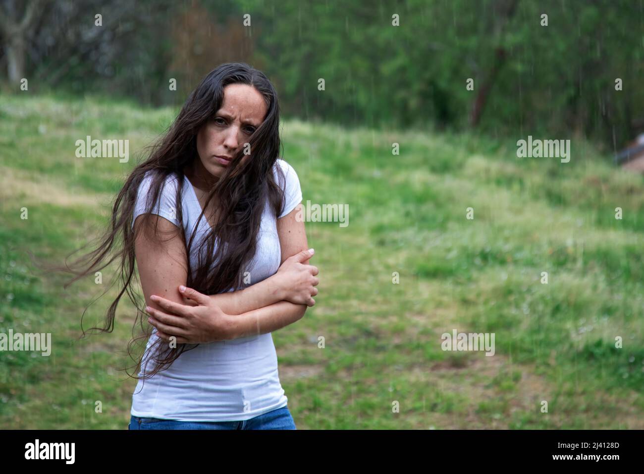 Langhaarige Brünette Frau im Regen umarmt sich. Traurigkeit, Depression und Angst. Konzept der Einsamkeit. Psychische Gesundheit. Suizidprävention Stockfoto