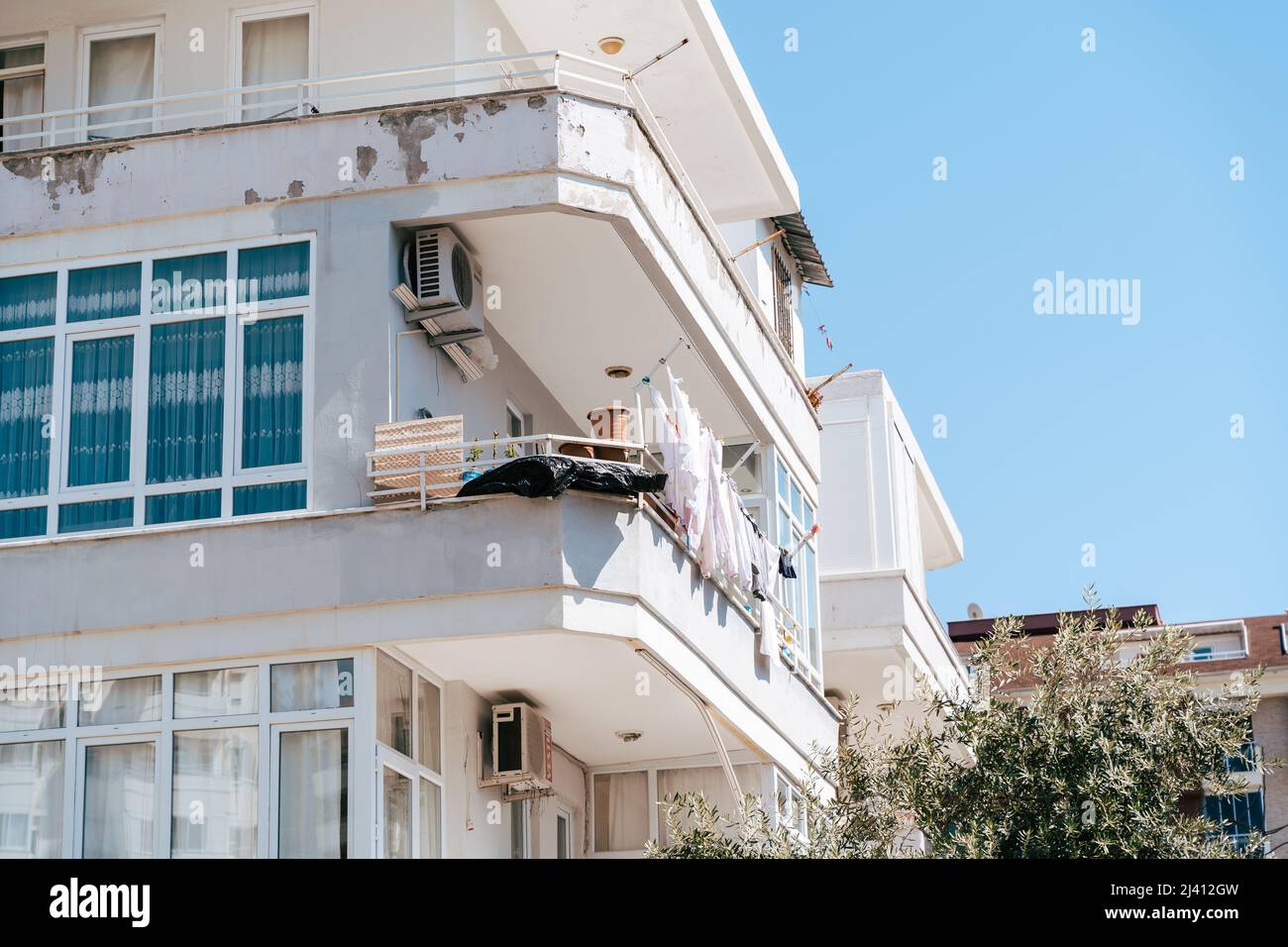 Weißes, heruntergekommenes, heruntergekommenes Wohnhaus mit Trocknungskleidung auf dem Balkon. Einfache Menschen leben. Abgewetzte, abgenutzte Wohnanlage mit alter Luft Stockfoto