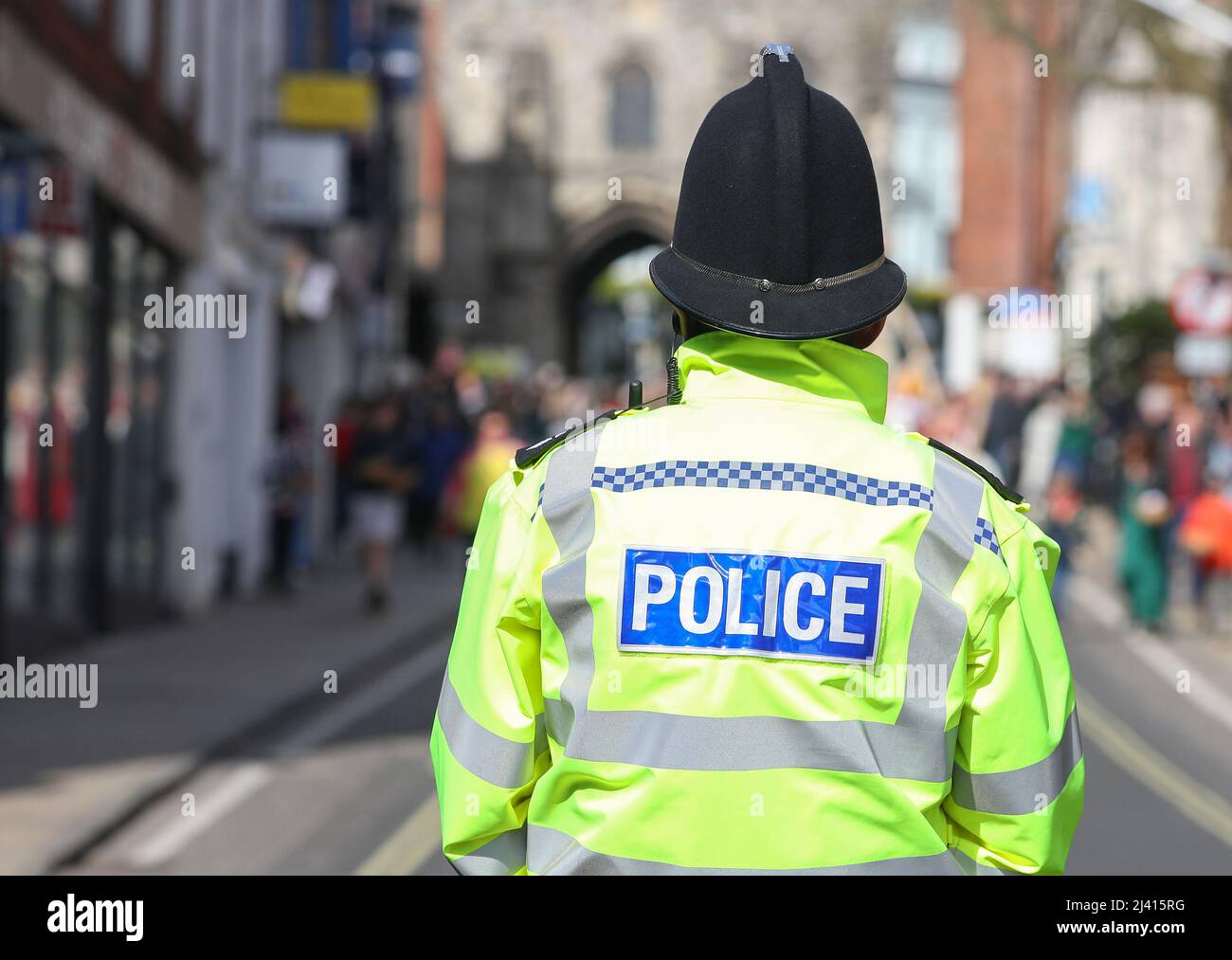 Ein Polizeibeamter aus Hampshire, der in Winchester im Vereinigten Königreich eine Jacke mit hoher Visibilde und einen traditionellen Polizeihelm trägt, der von hinten abgebildet ist. Stockfoto