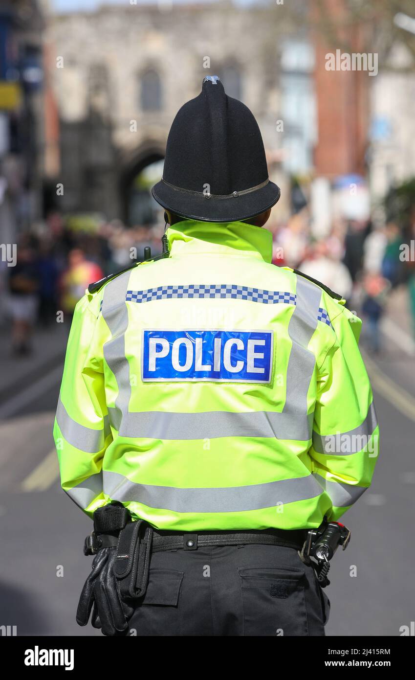 Ein Polizeibeamter aus Hampshire, der in Winchester im Vereinigten Königreich eine Jacke mit hoher Visibilde und einen traditionellen Polizeihelm trägt, der von hinten abgebildet ist. Stockfoto