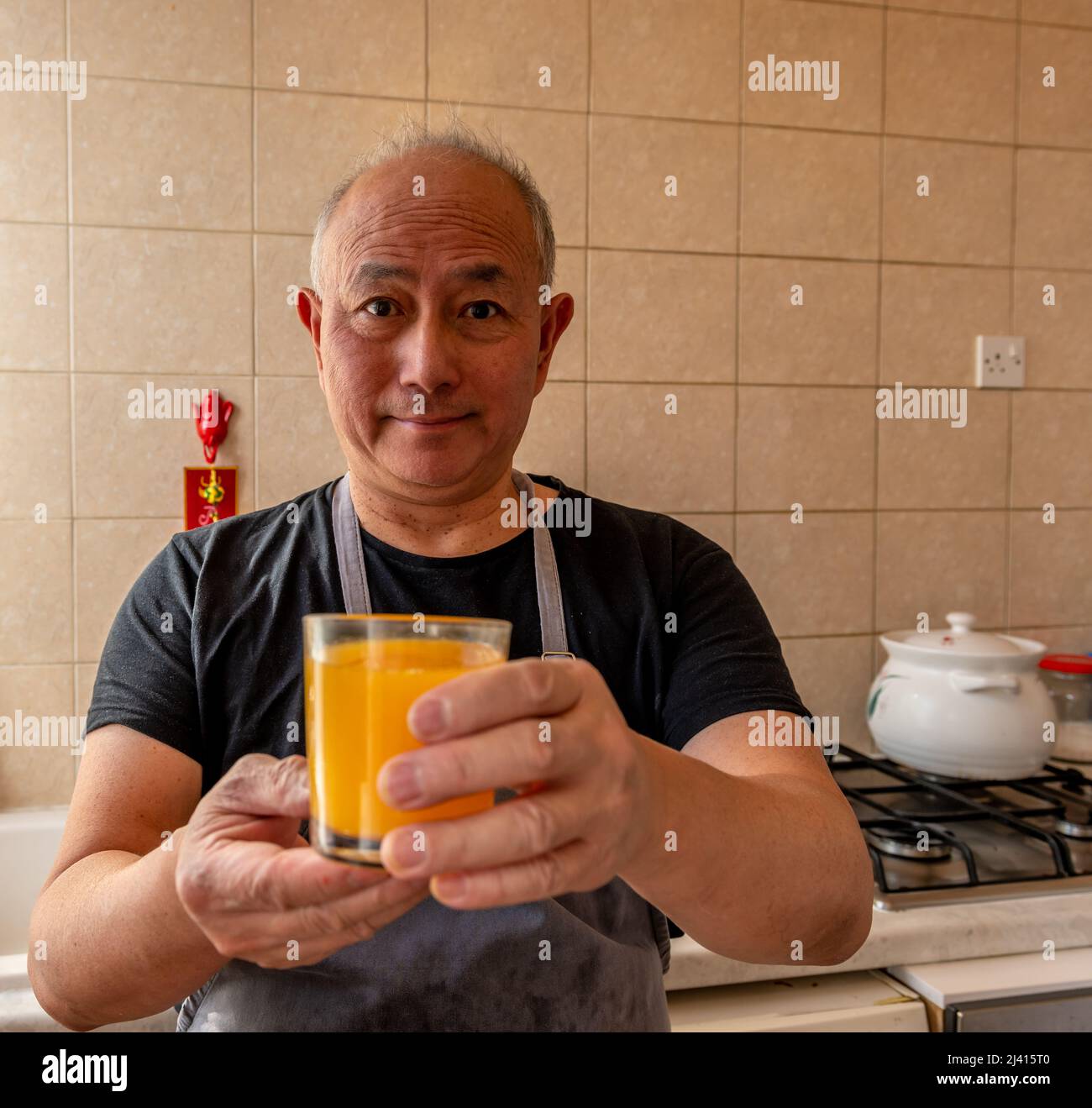 Ein älterer Koch präsentiert ein Glas frisch gepressten Orangensaft. Stockfoto