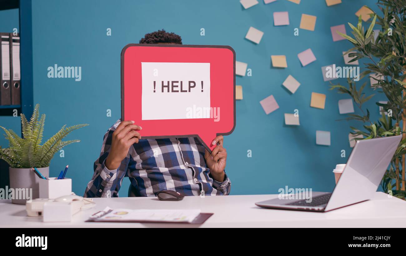 Verwirrter Mann mit Sprechblase, um Hilfe zu bitten, der an einem Laptop für Führungskräfte arbeitete. Person, die ein Kartentafel-Banner mit einer Textnachricht auf der Kamera verwendet und das Kommunikationssymbol anzeigt. Stockfoto