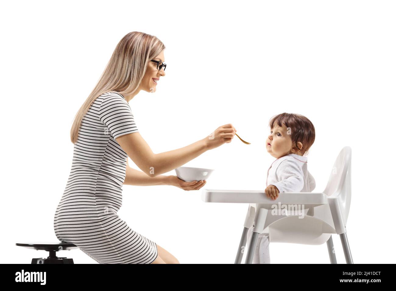Mutter füttert ein Baby, das auf einem Stuhl auf weißem Hintergrund sitzt Stockfoto