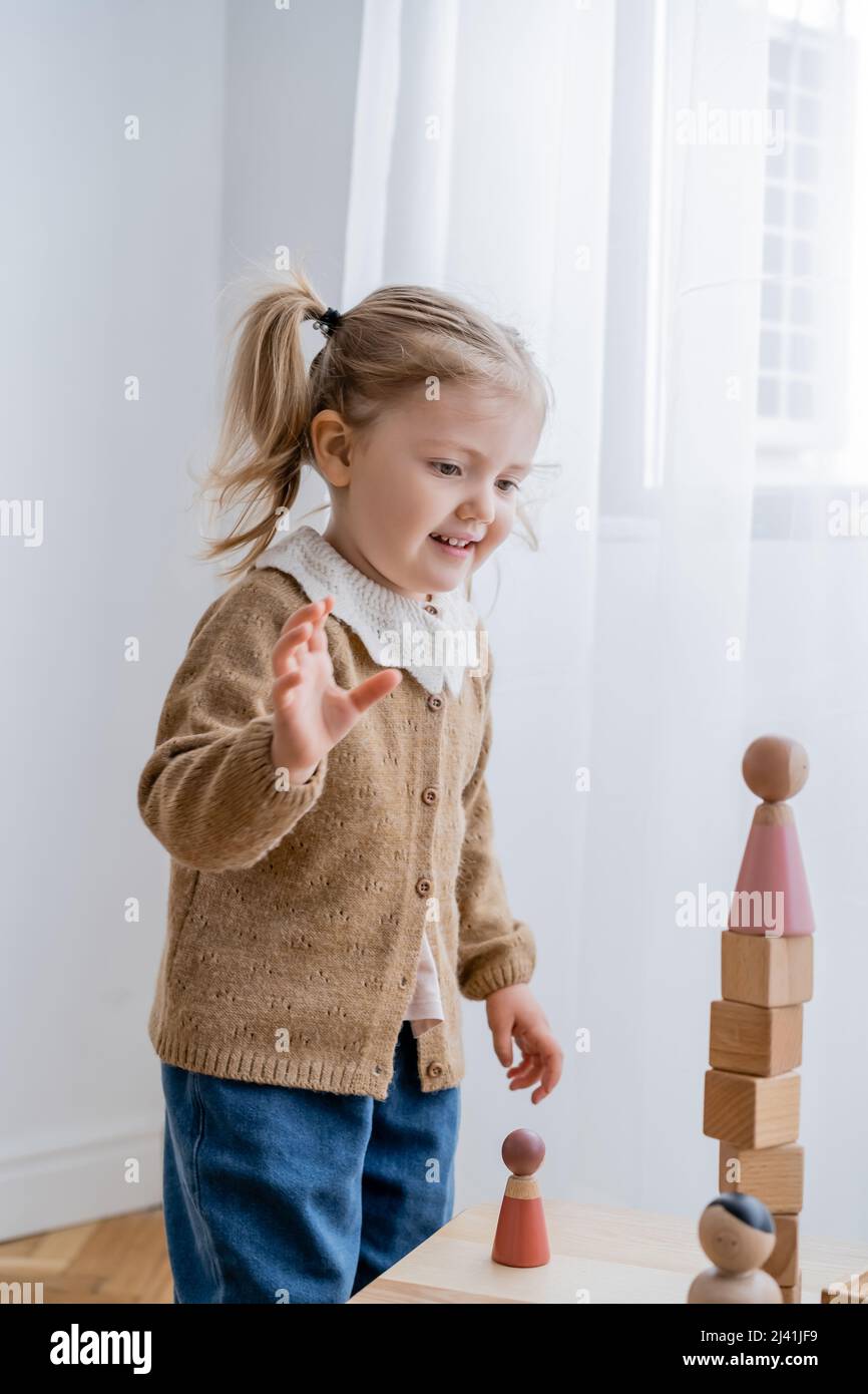 Glückliches Mädchen, das beim Spielen zu Hause einen Turm aus Holzwürfeln und Figuren ansieht Stockfoto