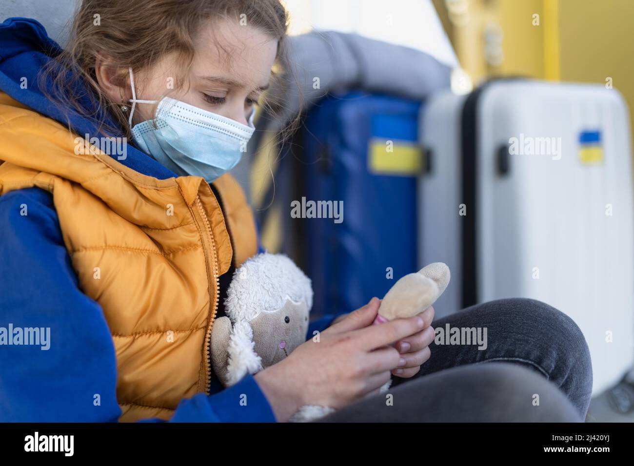 Trauriges ukrainisches Flüchtlingskind mit Gesichtsmaske wartet am Bahnhof, ukrainisches Kriegskonzept. Stockfoto