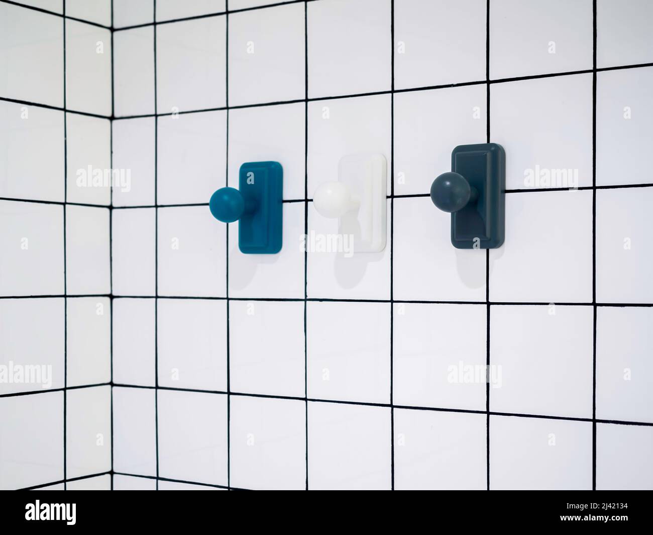 Leere drei moderne Handtuchhaken, blau und weiß hängen auf weißen Gitterwand Badezimmer Hintergrund mit Kopierer Platz, minimalistischen Stil. Stockfoto