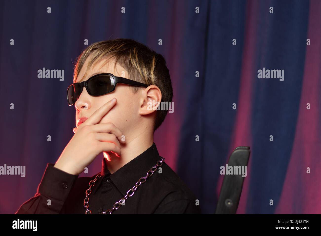 Porträt eines stilvollen Teenagers von 13 Jahren mit einer modischen Frisur in schwarzer Sonnenbrille mit einer Kette um den Hals auf violettem Hintergrund. Sele Stockfoto