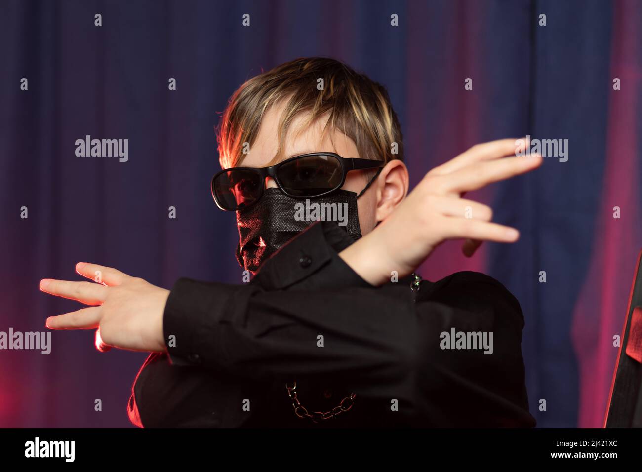 Porträt eines stilvollen Teenagers 13 Jahre alt mit einer modischen Frisur in schwarzer Sonnenbrille, einer Schutzmaske und mit einer Kette um den Hals auf einem Stockfoto