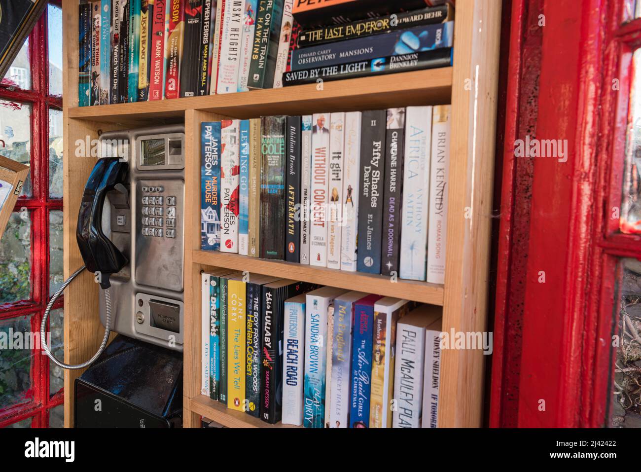 Bücher, die in einem roten Telefonkasten in Regalen angeordnet sind, können ausgeliehen werden. Stockfoto
