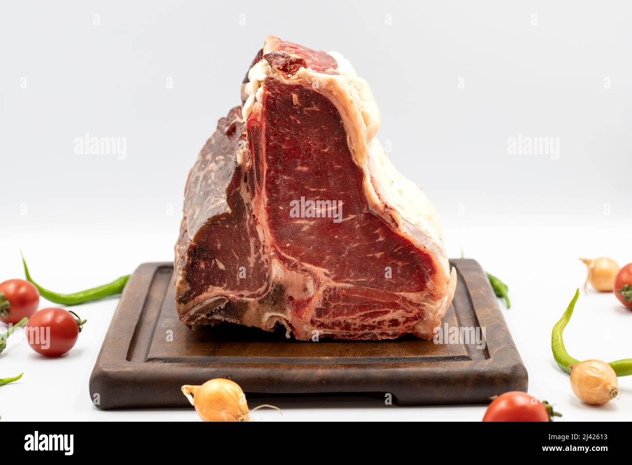 Trocken gereiftes Roh-T-Bone- oder Porterhouse-Rindfleisch-Steak mit Tomaten und Paprika. Weißer Hintergrund. Yakın çekim Stockfoto