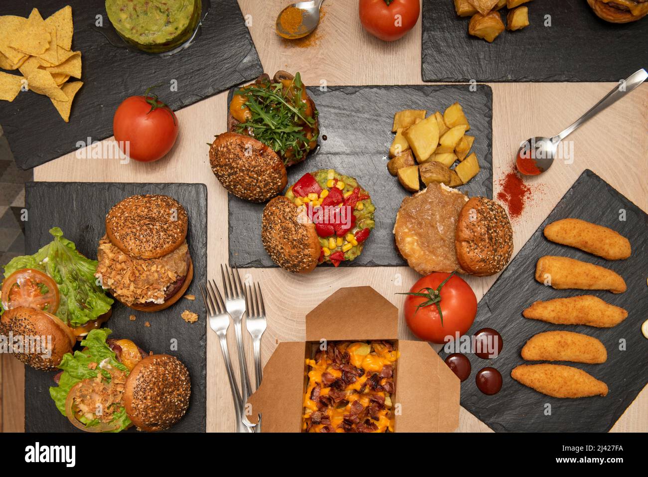 Fastfood-Gerichte mit verschiedenen Hamburgern, hausgemachten Pommes frites, Hähnchenfingern, Kartoffeln mit Frischkäse und Schinkentacos, Nachos mit Guacamole und frisch Stockfoto