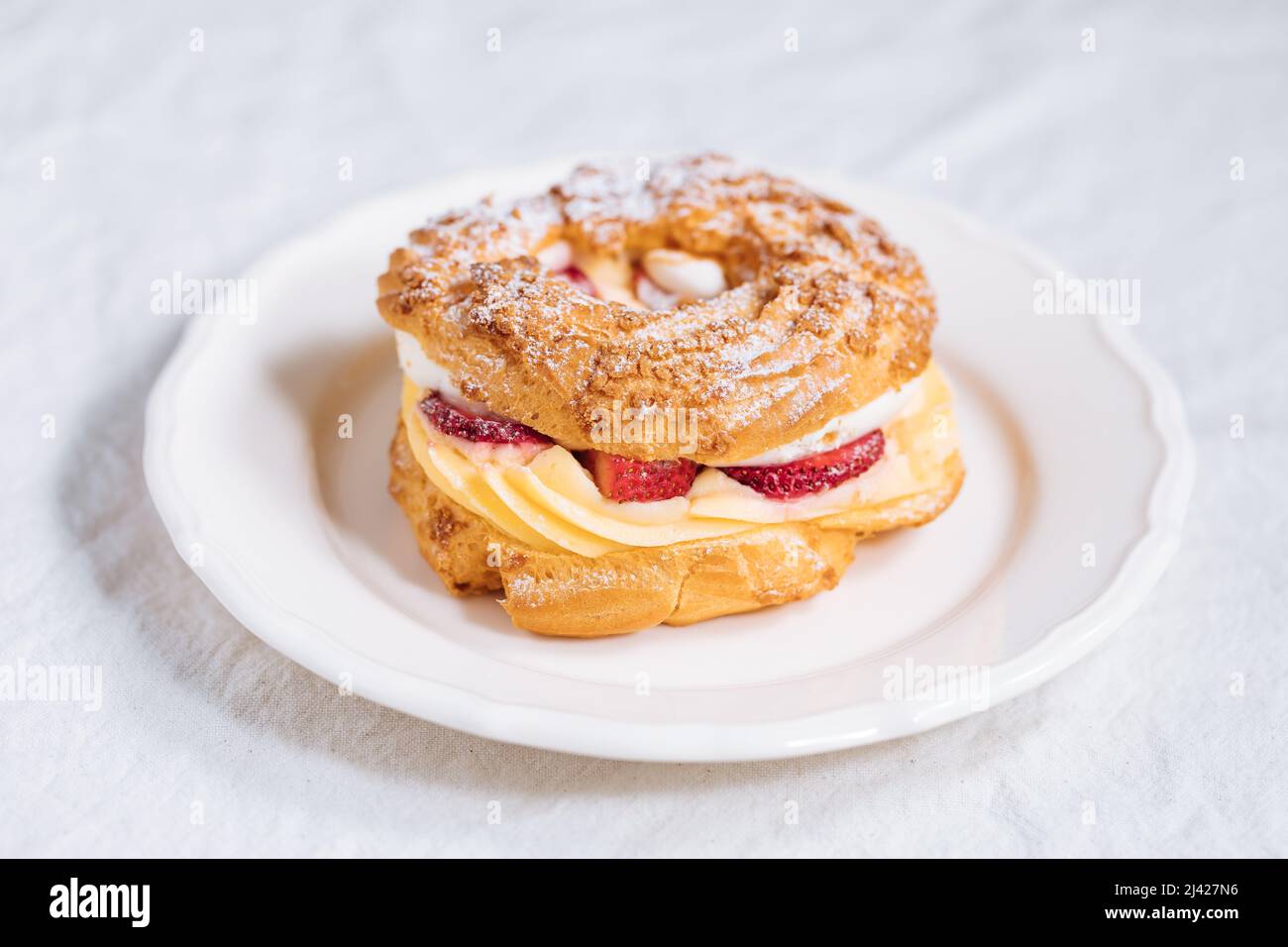 Traditionelles französisches Dessert namens Paris Brest auf hellgrauem Hintergrund mit Puderzucker und Erdbeeren Stockfoto