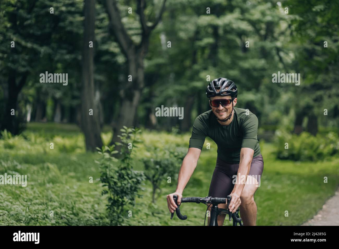 Glücklicher aktiver Mann mit professionellem Fahrrad für intensives Training im Stadtpark. Der kaukasische Sportler trägt Sportkleidung, Schutzhelm und Spiegelglas Stockfoto