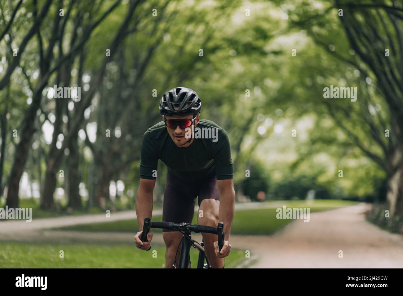 Fitness junger Mann, der Freizeit zum Radfahren im Sommerpark verbringt. Der kaukasische Sportler trägt Sportkleidung, Helm und Brille. Aktivitäten im Freien Stockfoto