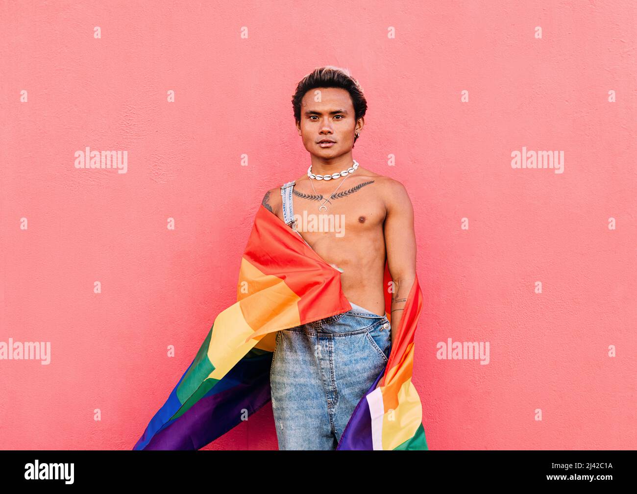 Junger ernsthafter Mann, der draußen mit Regenbogenfahne steht Stockfoto