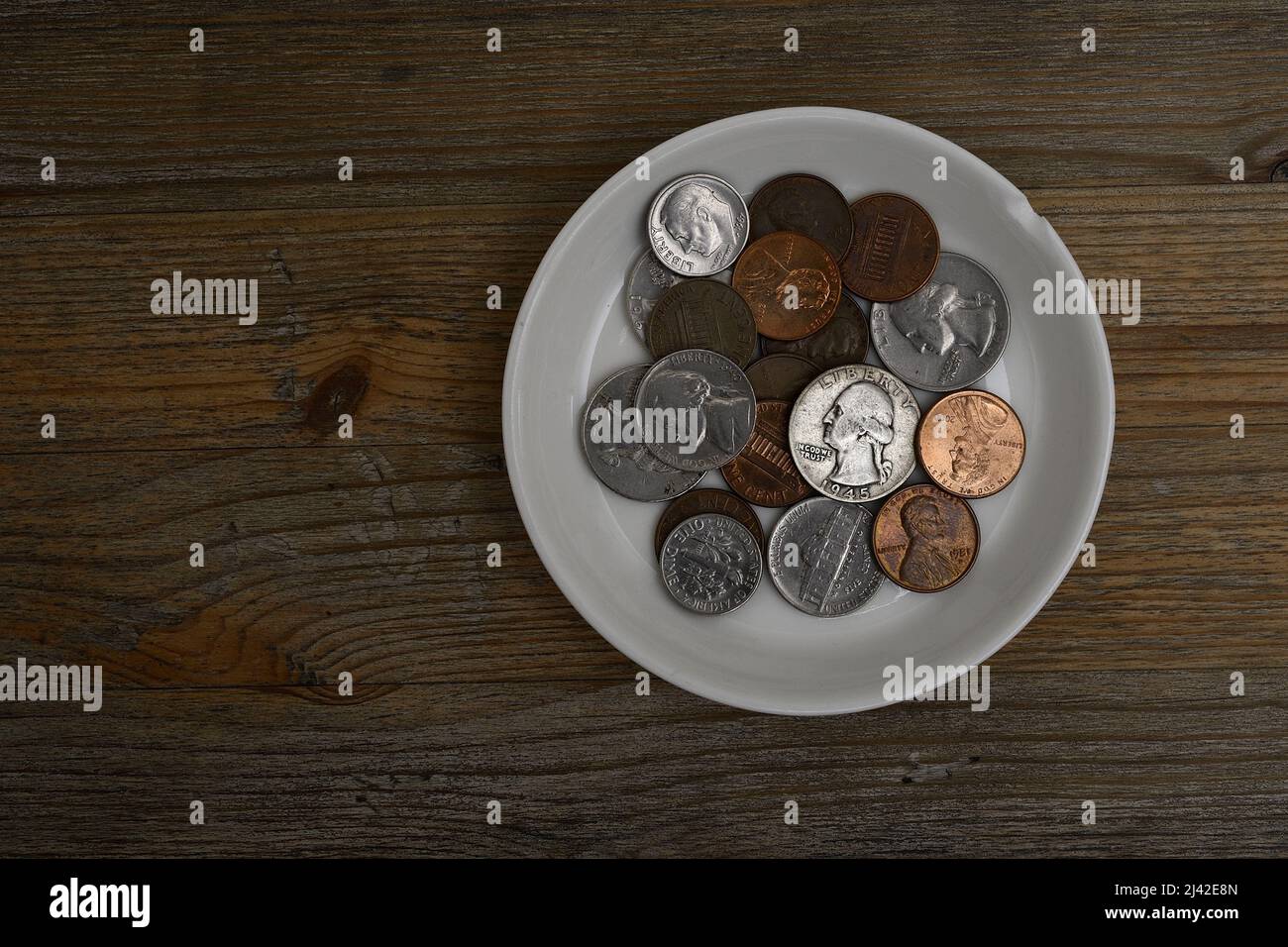 Kleine amerikanische Münzen auf einer weißen Porzellanuntertasse auf einem Holztisch Stockfoto